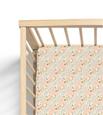A crib sheet with a floral pattern featuring sunflowers and other wildflowers, fitted on a crib with a wooden frame.
