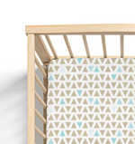 A fitted crib sheet with a contemporary geometric triangle pattern in shades of blue and brown, displayed on a crib with a wooden frame.