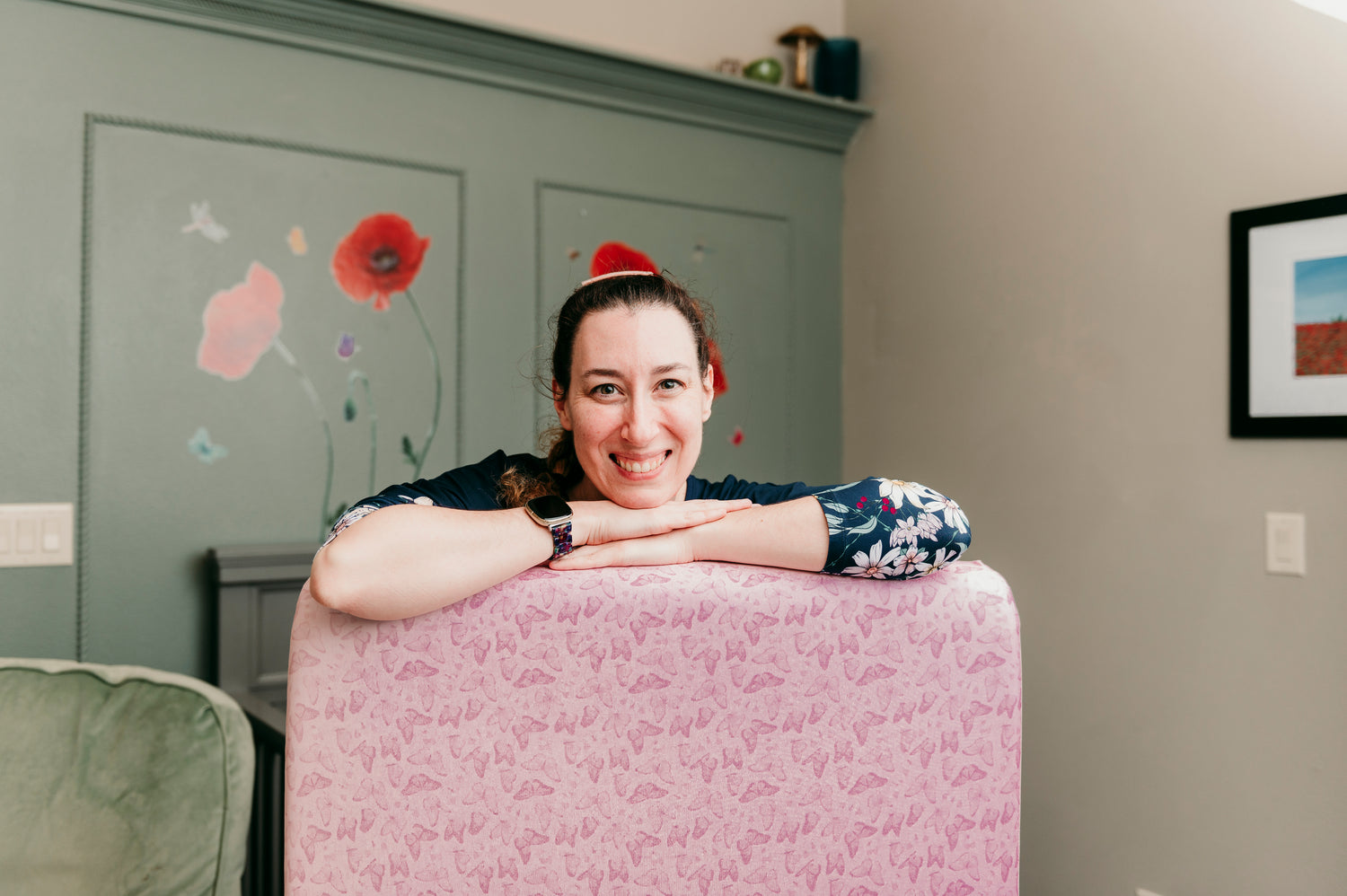 founder of cradle comforts co. leaning on crib sheet with butterflies on it