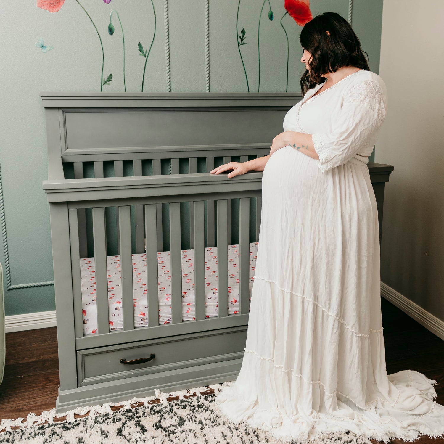 Expecting mother looking at crib with a mushroom crib sheet in a room decorated with poppies and green accent wall