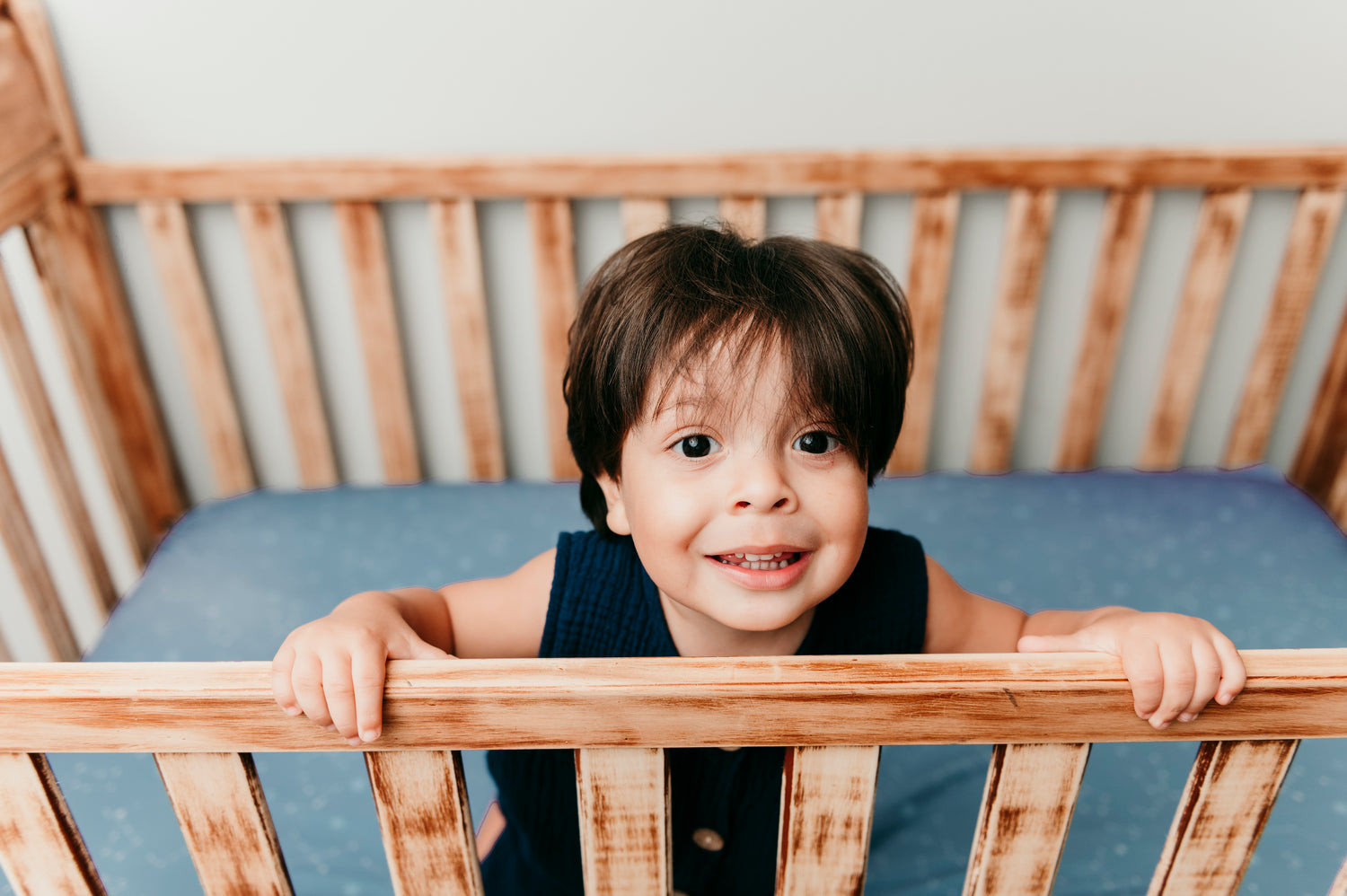 cute baby standing in crib with a celestial sheet on the mattress