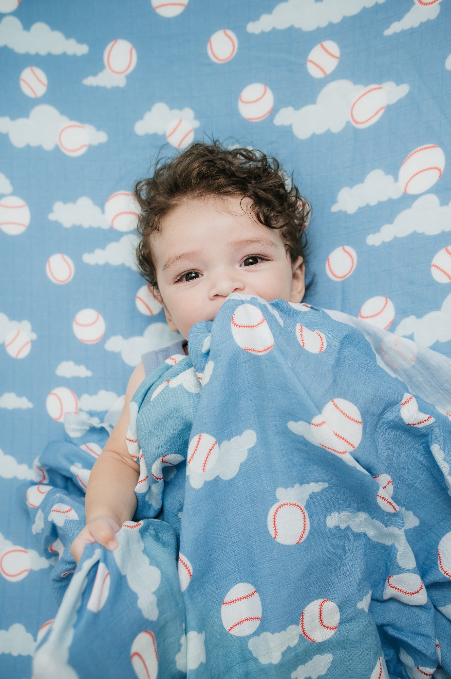 Child wrapped in a blue blanket with baseball pattern on a matching background