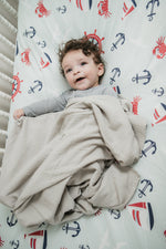 Baby wrapped in a beige blanket on a crib with nautical-themed bedding
