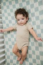 Baby lying on a checkered sheet wearing a beige outfit