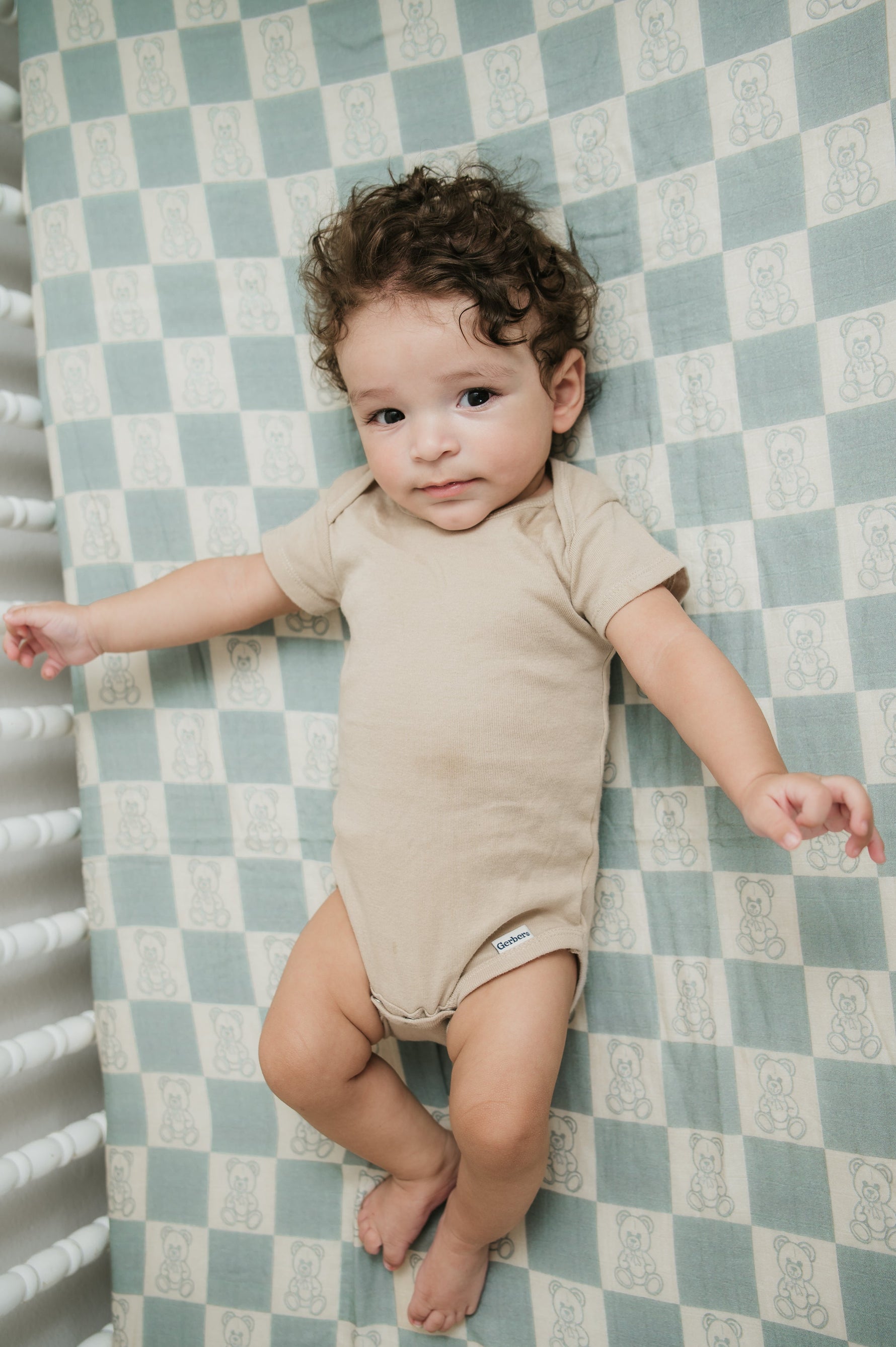 Baby lying on a checkered sheet wearing a beige outfit