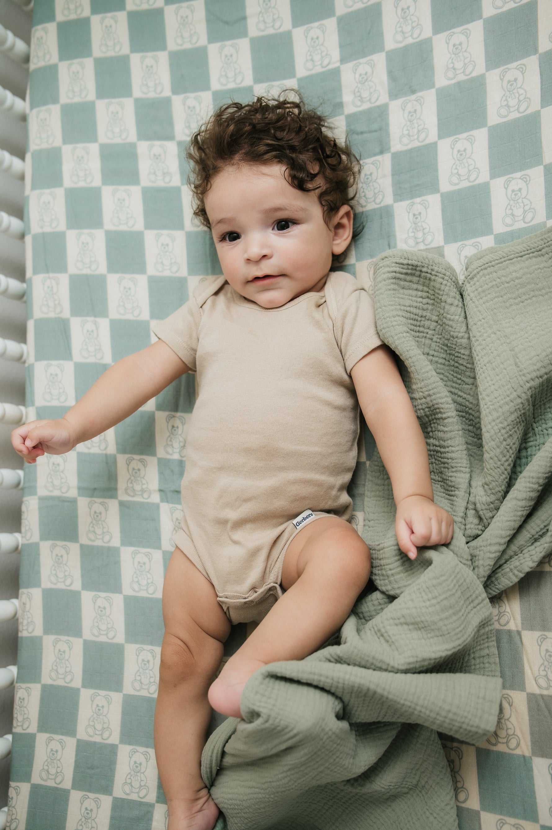 Baby lying on a checkered sheet with a green blanket
