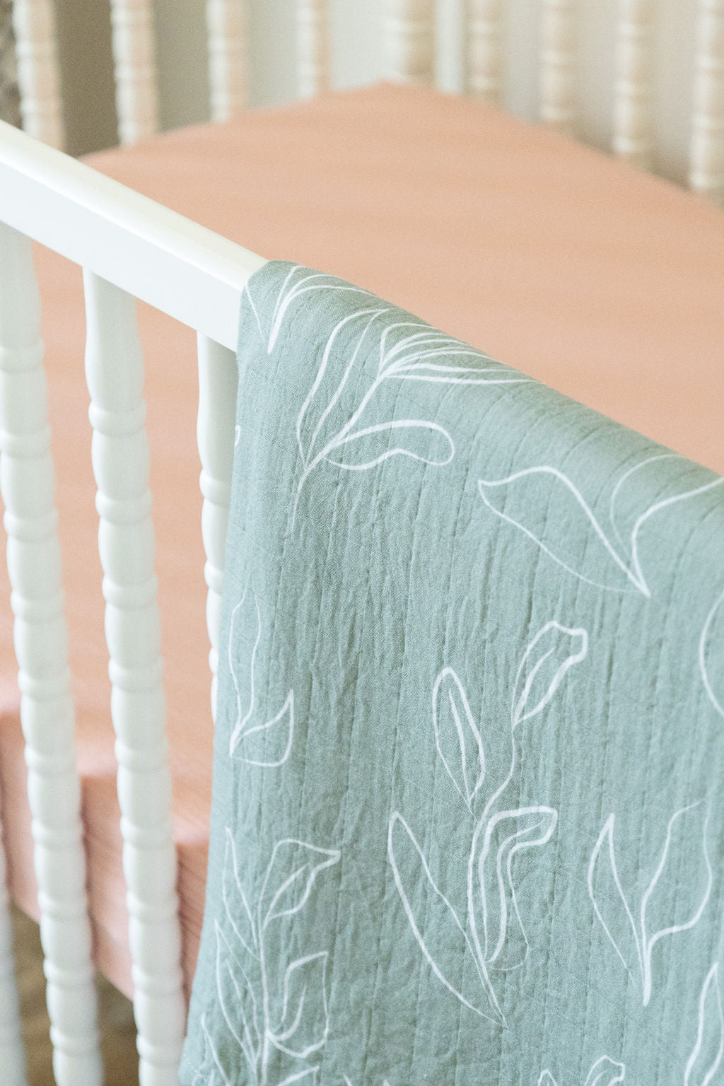 Green textured blanket with white leaf patterns draped over a crib.