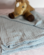 Plush toy horse on a textured blanket with a blurred background