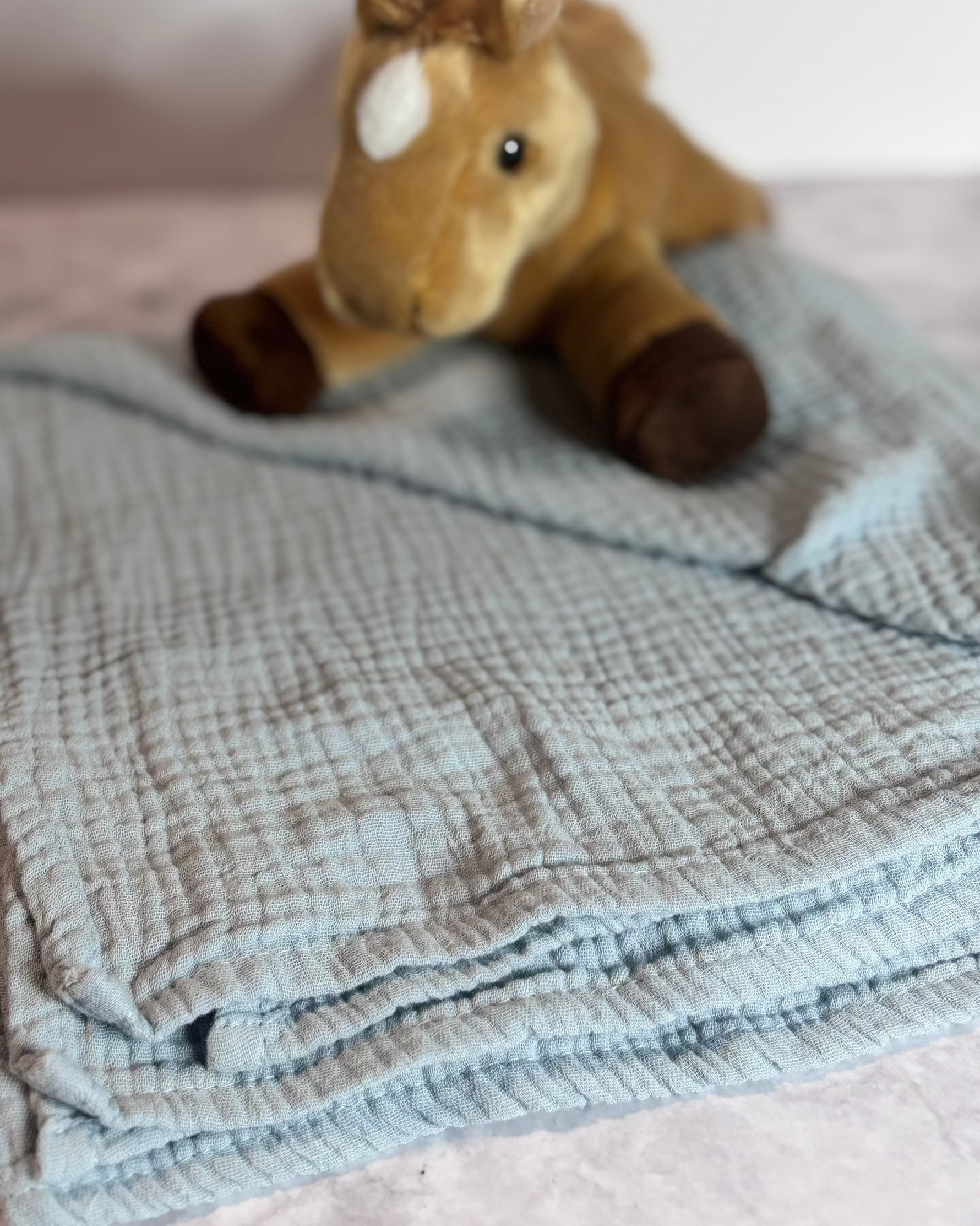 Plush toy horse on a textured blanket with a blurred background