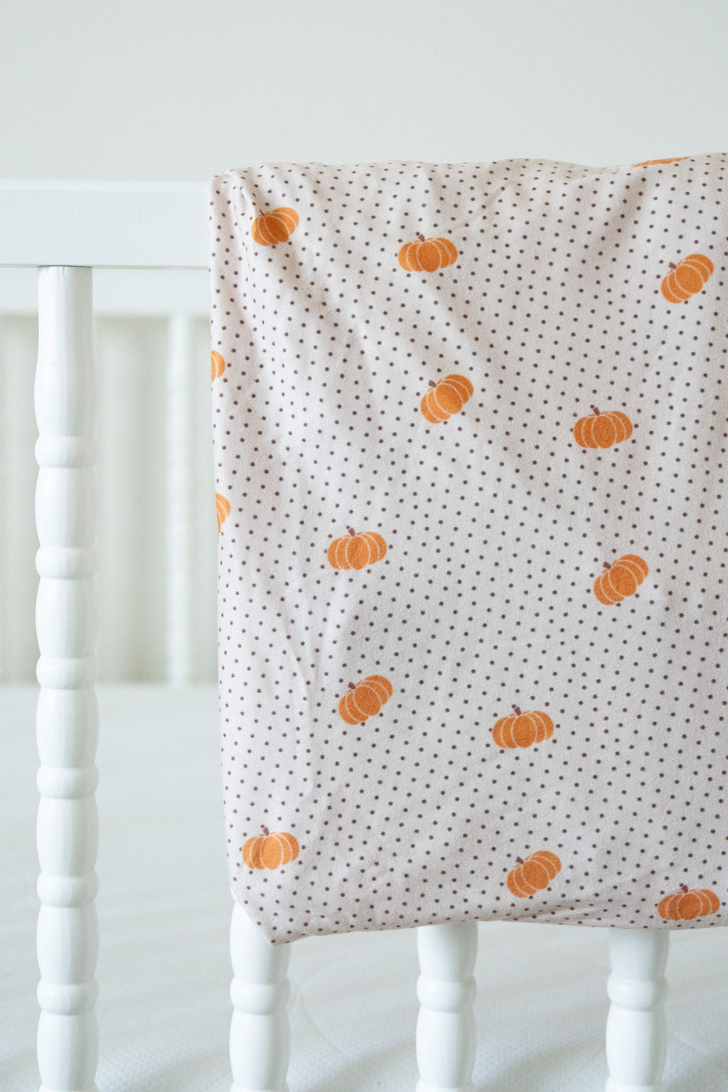 Crib sheet with pumpkin pattern draped over a white crib