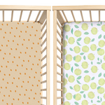Two crib sheets with pumpkin patterns and apples pattern on a wooden crib.